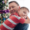Portrait of a smiling father hugging his young son while standing in front of a Christmas tree during the holidays